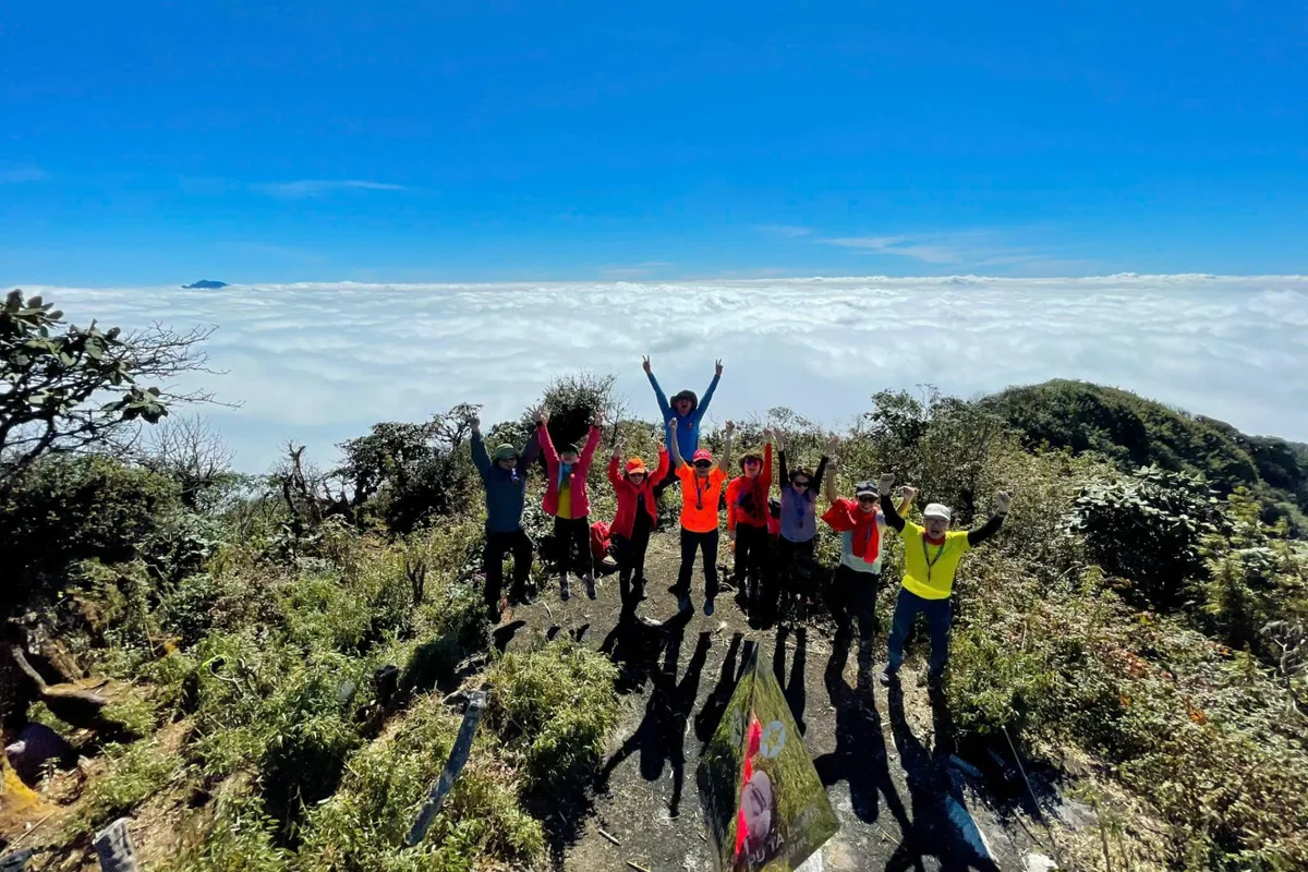 Student group celebrating on a mountain summit above the clouds in Vietnam